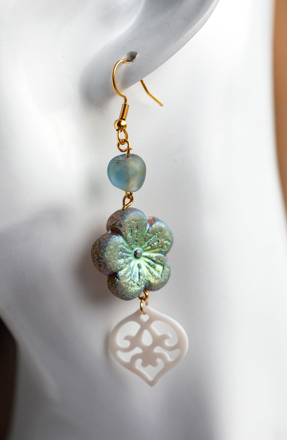 handmade dangle drop earrings featuring a Czech glass gold hibiscus bead in etched matte smoke, an African recycled glass bead in blue/brown and a carved freshwater shell heart. finished with gold-plated stainless steel findings 