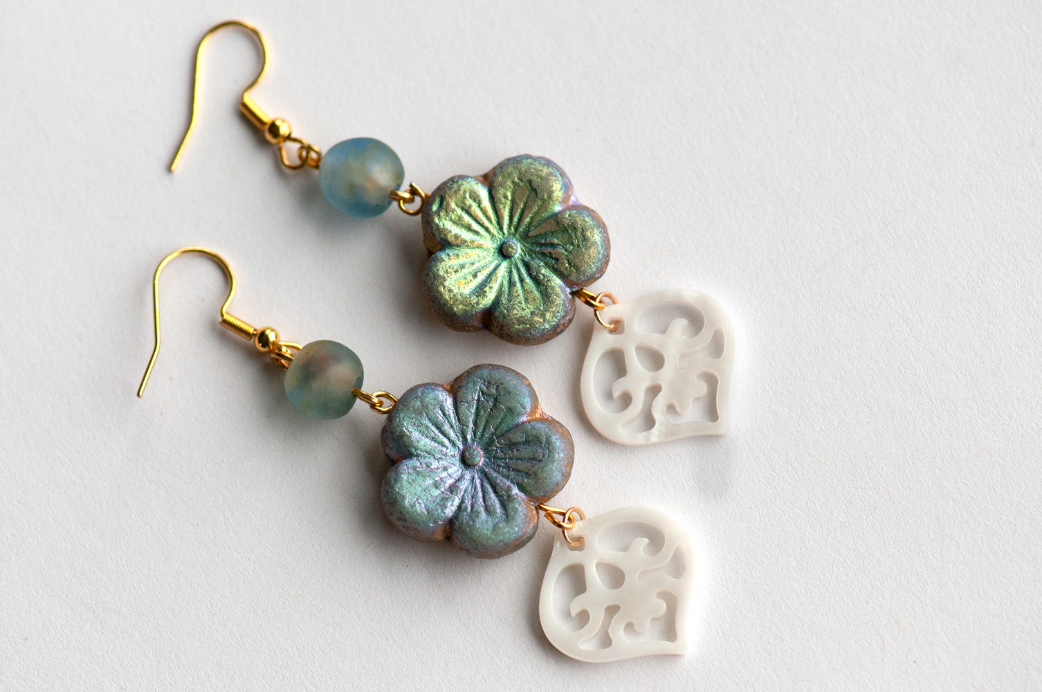 handmade dangle drop earrings featuring a Czech glass gold hibiscus bead in etched matte smoke, an African recycled glass bead in blue/brown and a carved freshwater shell heart. finished with gold-plated stainless steel findings 