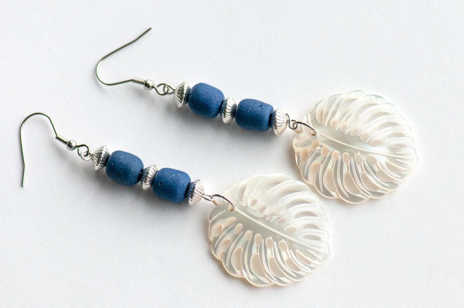 Daring dangle earrings featuring mother-of-pearl carved palm leaves accented with cobalt blue African recycled glass beads and silver-plated accents