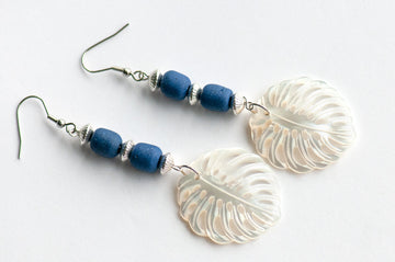 Daring dangle earrings featuring mother-of-pearl carved palm leaves accented with cobalt blue African recycled glass beads and silver-plated accents