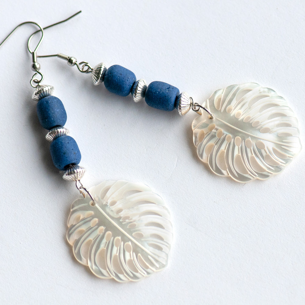Daring dangle earrings featuring mother-of-pearl carved palm leaves accented with cobalt blue African recycled glass beads and silver-plated accents