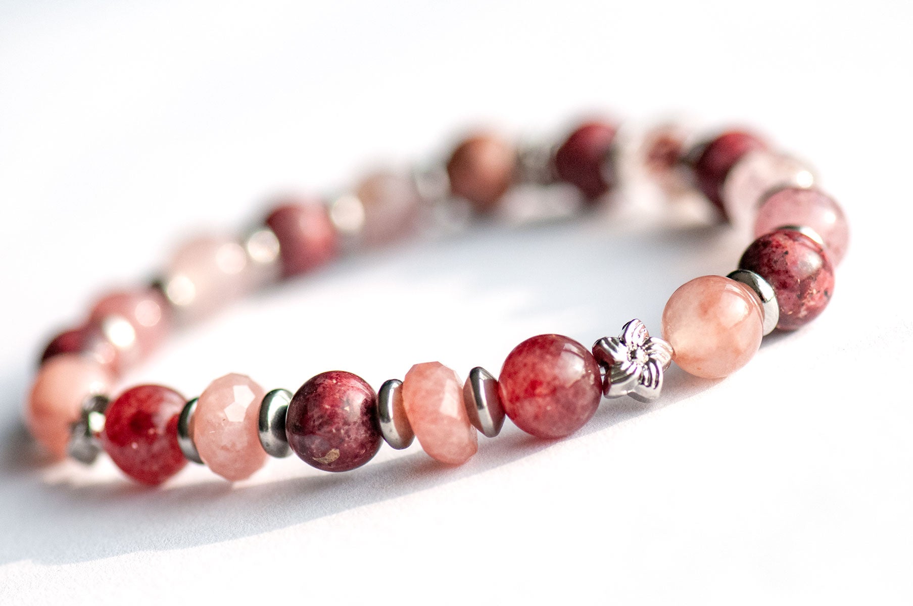 Carnation January birth flower focal bracelet — side view, showing depth and sparkle of Eudialyte and Strawberry Quartz rounds with platinum flower spacers