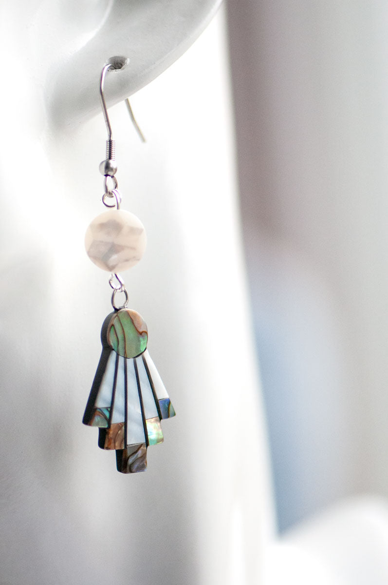 A close-up of the Fierce Lynx Designs Mother of Pearl Flare Earrings, featuring a round, pearl-like bead and a fan-shaped shell design, dangling elegantly from the ear.