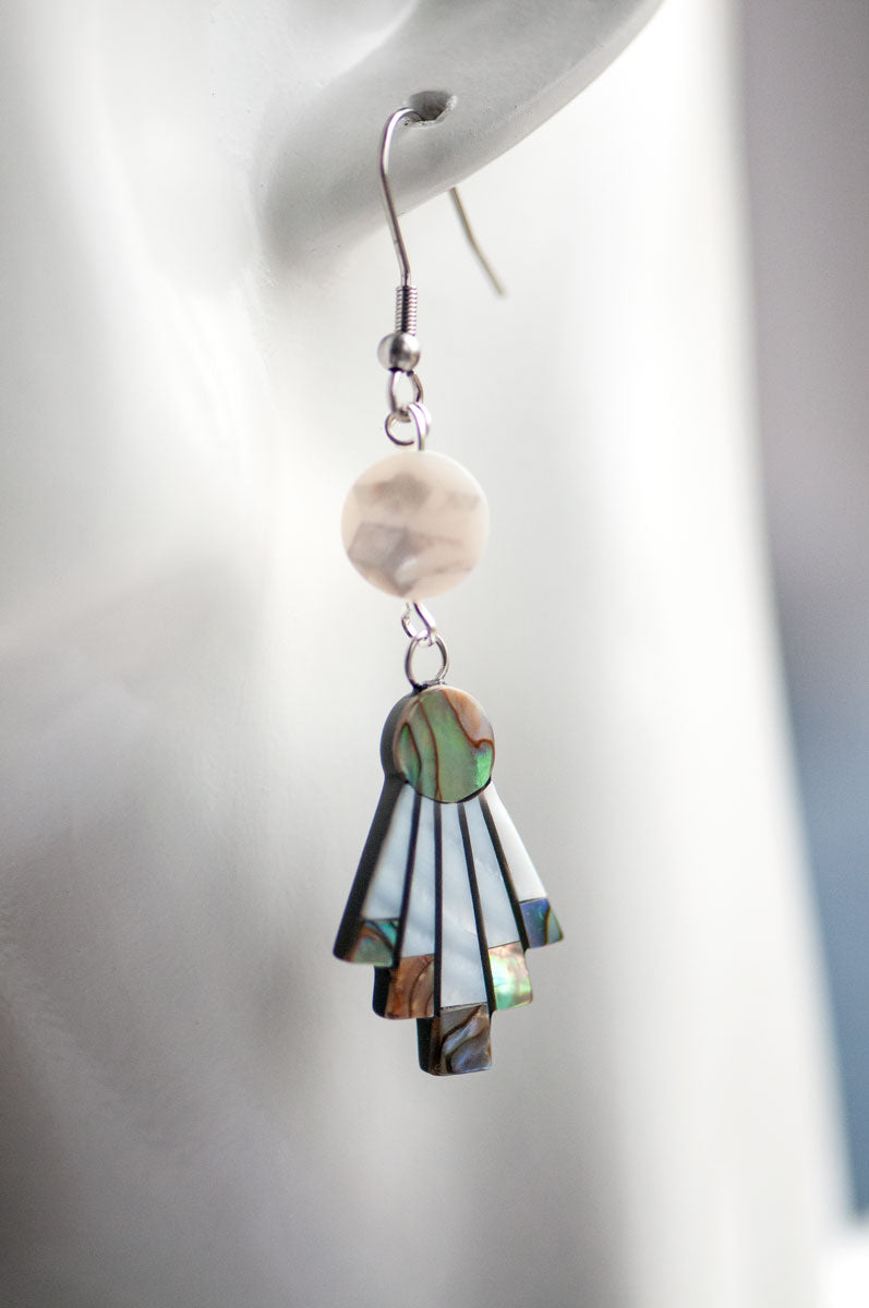 A close-up of a mannequin ear wearing the Mother of Pearl Flare Earrings by Fierce Lynx Designs, featuring an iridescent statement design with a round white bead and a fan-shaped, multicolored abalone shell pendant.