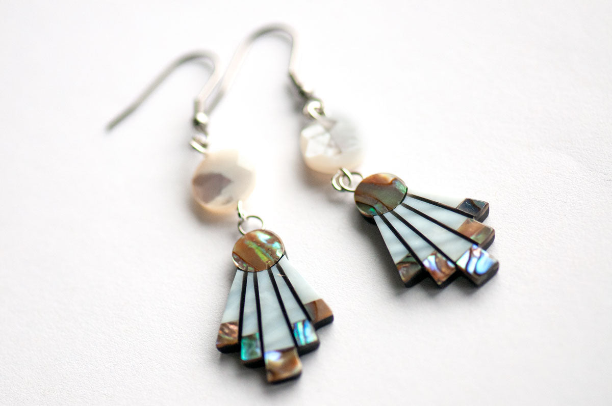 The Mother of Pearl Flare Earrings by Fierce Lynx Designs are striking statement pieces, showcasing fan-shaped abalone shell inlays and faceted round white stones, beautifully arranged against a crisp white background.
