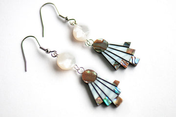 The Mother of Pearl Flare Earrings by Fierce Lynx Designs feature two dangling earrings with round white beads and fan-shaped iridescent abalone shell accents, displayed on a white background.