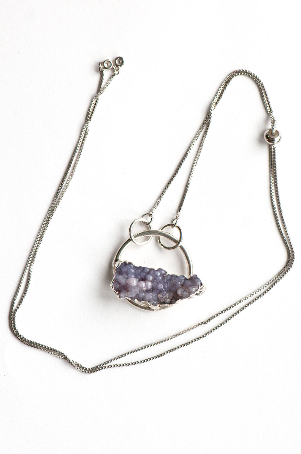 Flat lay of a Purple Grape Agate hoop pendant on a silver box chain with the adjustable slider bead and crystal-tipped ends.