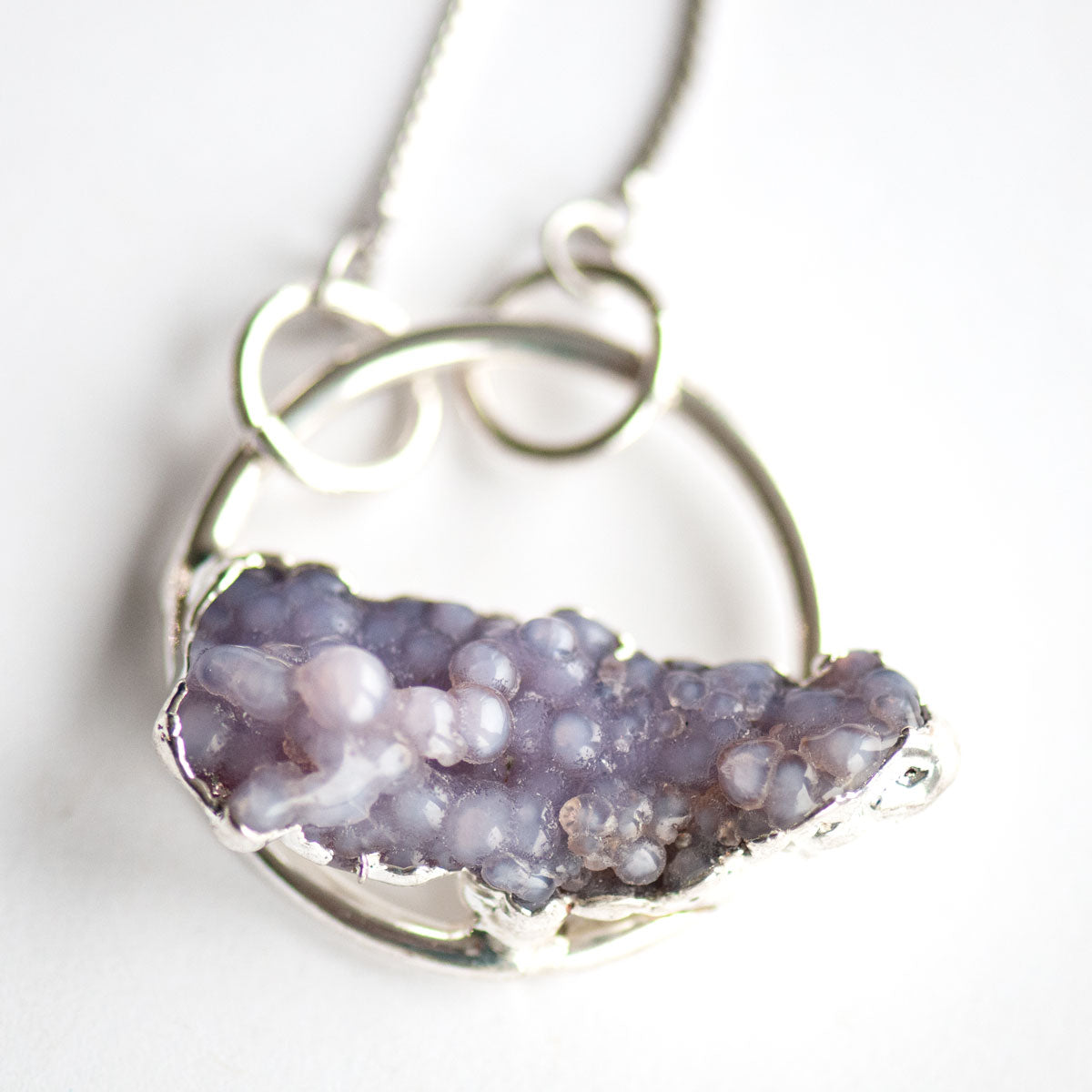 Close-up of the translucent lavender spheres of a Purple Grape Agate pendant in an electroformed silver hoop.