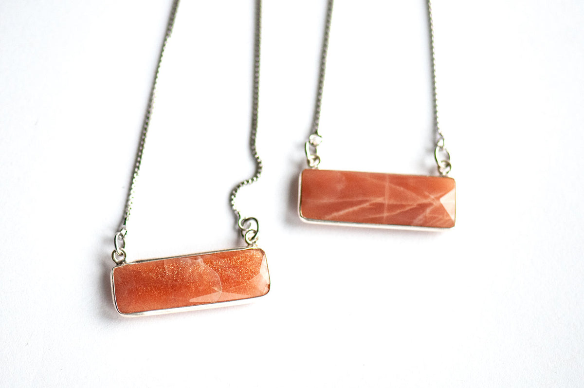 Two faceted peach gemstone bar pendants on silver box chains, one with a copper sparkle and one with a soft silvery sheen.