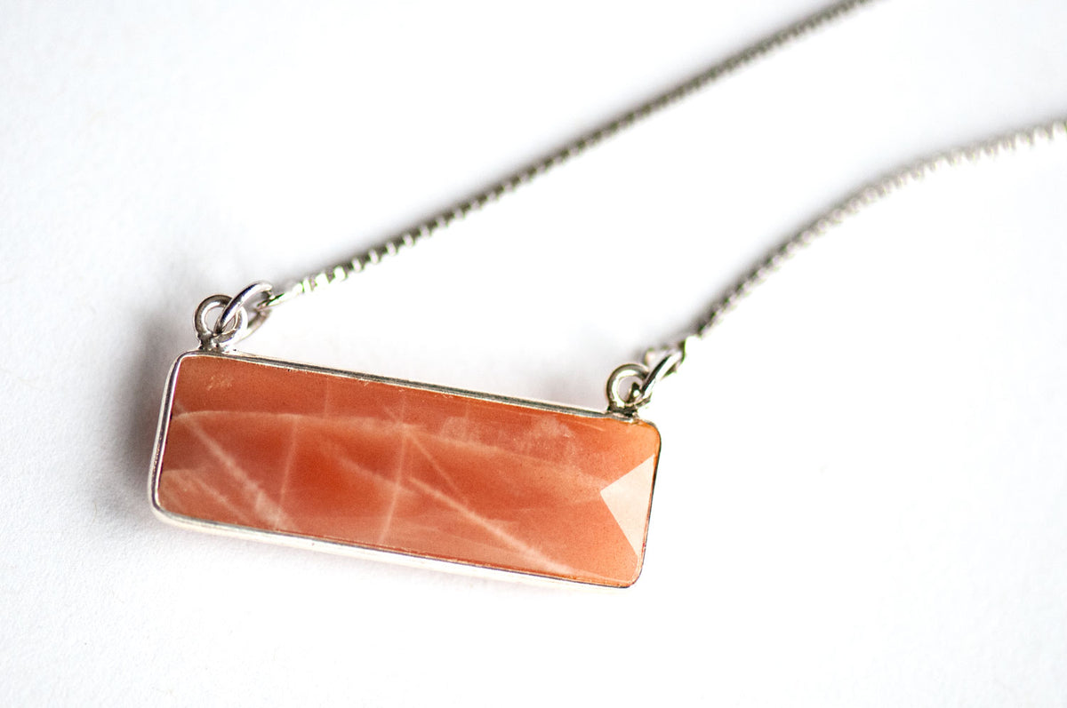 Close-up of a faceted Peach Moonstone bar pendant in a silver bezel, with white sheen lines across the stone.