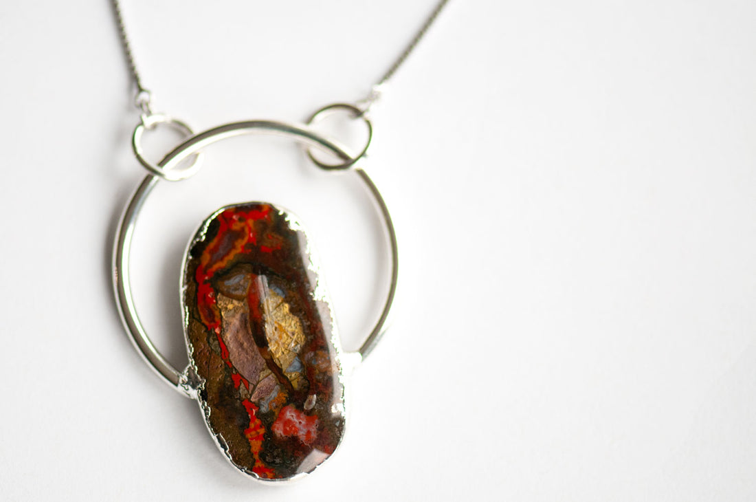 Close-up of a Moroccan Seam Agate cabochon with bright red seams, gold and lavender patches, edged in electroformed silver inside an open hoop.