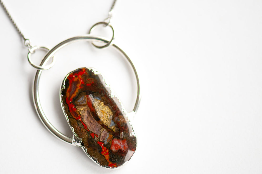 Close-up of a Moroccan Seam Agate cabochon with bright red seams, gold and lavender patches, edged in electroformed silver inside an open hoop.