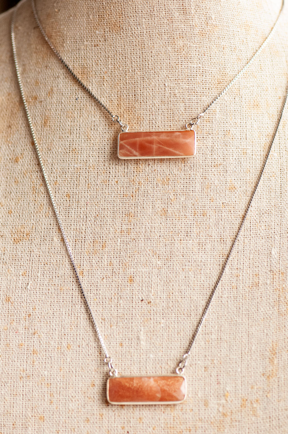 Two peach gemstone bar pendant necklaces layered on a linen bust, one at choker length and one longer.