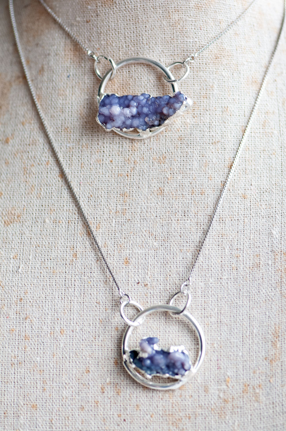Two Purple Grape Agate pendant necklaces layered on a linen bust, one at choker length and one longer.