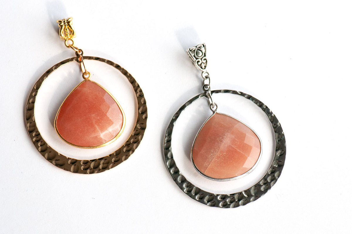 Sunlit Lynx pendants side by side in gold and silver, each a faceted Peach Moonstone pear in a wide hammered ring.