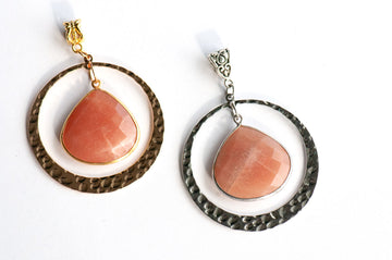 Sunlit Lynx pendants side by side in gold and silver, each a faceted Peach Moonstone pear in a wide hammered ring.