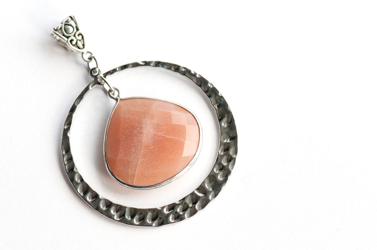 Angled view of the silver Sunlit Lynx pendant showing golden sparkle and soft sheen in the Peach Moonstone.