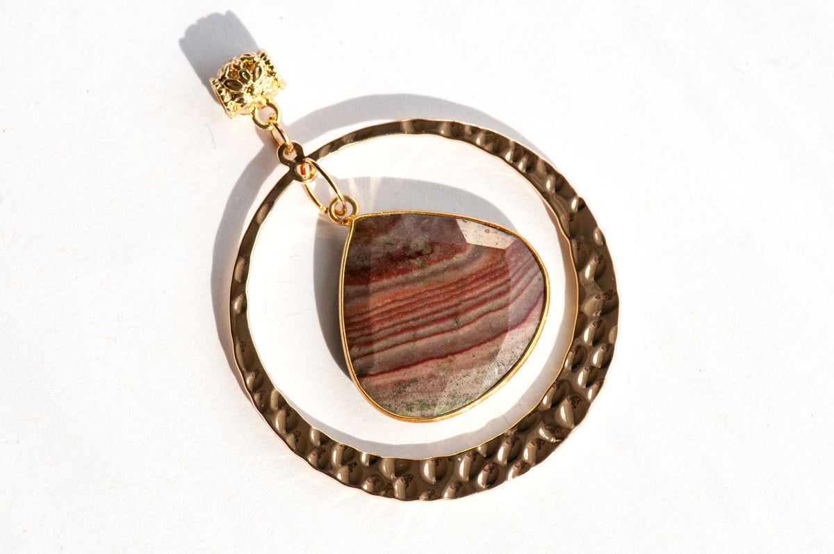 Fireside Lynx - Polychrome Jasper Pendant featuring a teardrop-shaped red and grey jasper stone hanging inside a textured, gold hammered hoop.