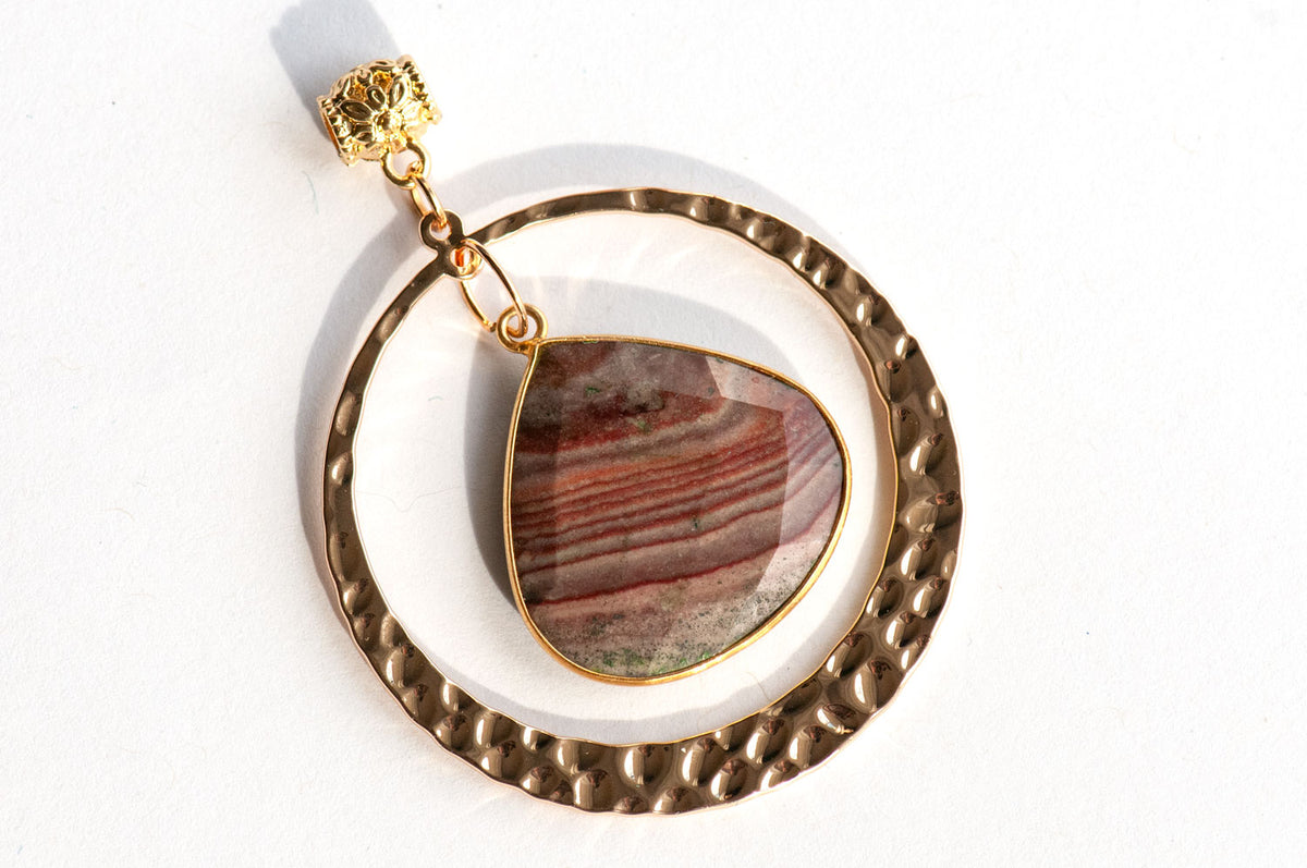 Fireside Lynx Polychrome Jasper Pendant featuring a teardrop-shaped stone with horizontal reddish-brown banding, suspended within a gold hammered metal circle.