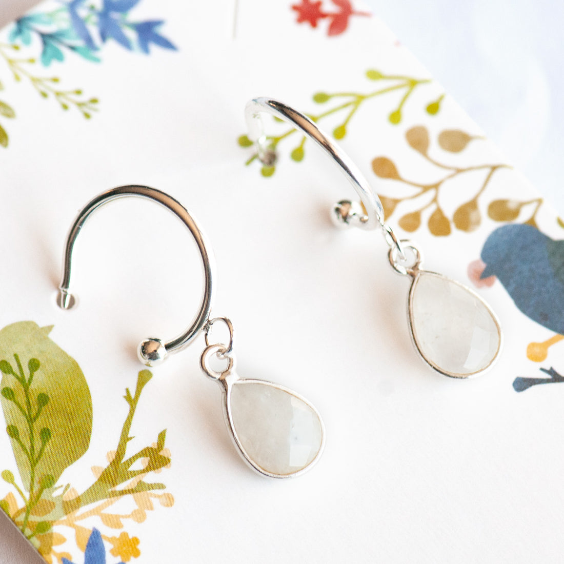 Stunning Sterling Silver bezel-faceted Rainbow Moonstone drops dangle from silver-plated stainless steel half hoop stud earrings. 