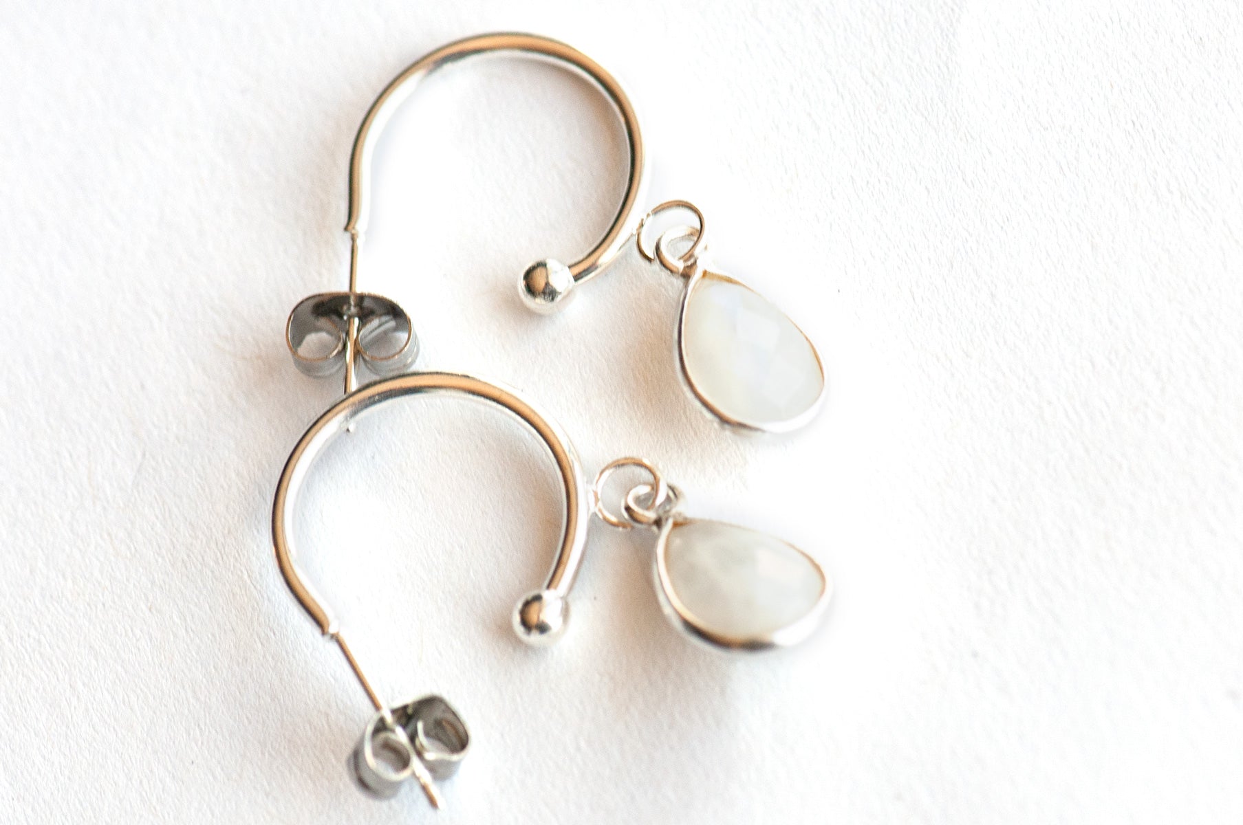 Stunning Sterling Silver bezel-faceted Rainbow Moonstone drops dangle from silver-plated stainless steel half hoop stud earrings. 