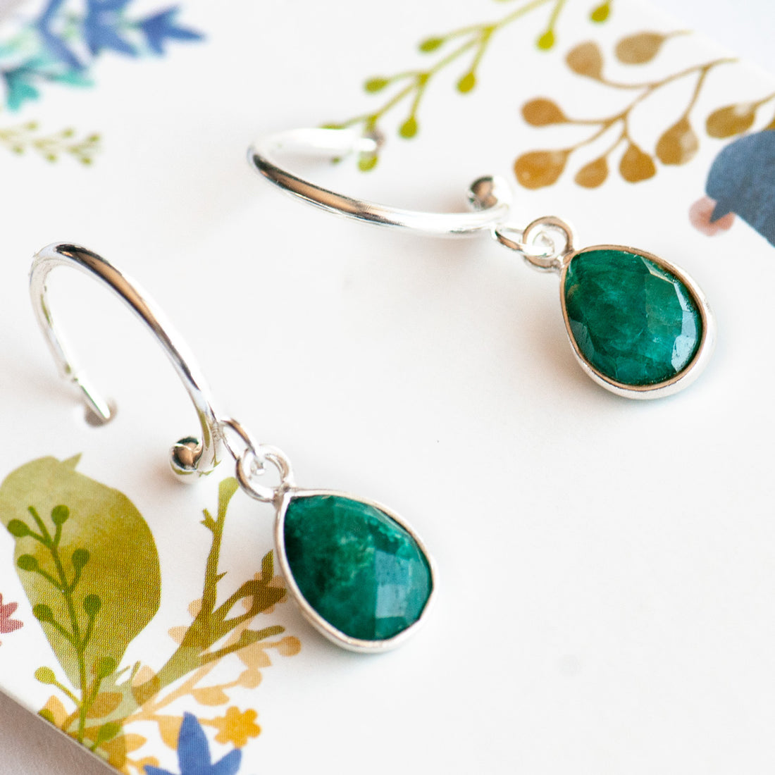 Stunning Sterling Silver bezel-faceted Emerald drops dangle from silver-plated stainless steel half hoop stud earrings. 