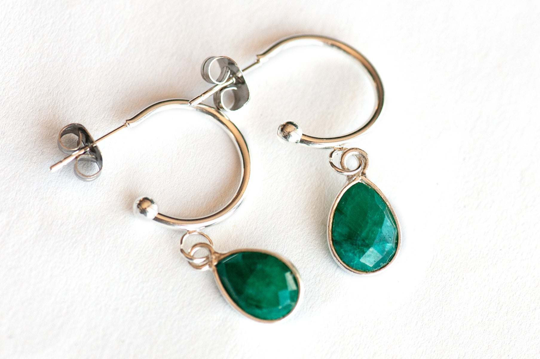 Stunning Sterling Silver bezel-faceted Emerald drops dangle from silver-plated stainless steel half hoop stud earrings. 
